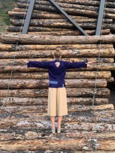 Modelo de espaldas luciendo una prenda de la marca Amarenak frente a una estructura de troncos de madera.
